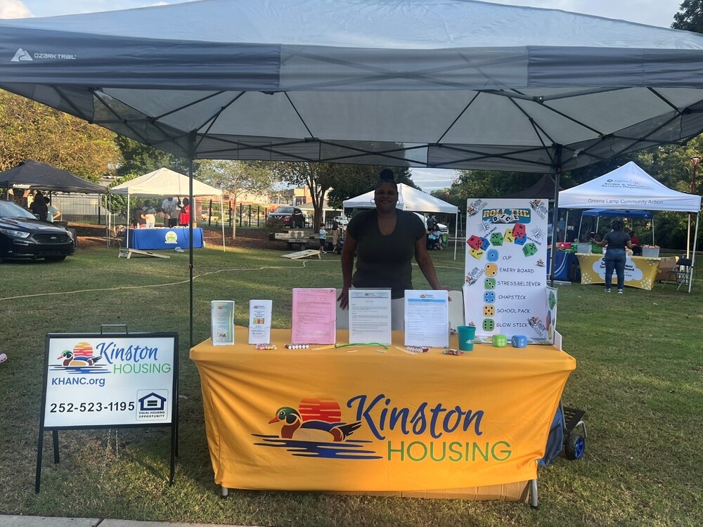 KHA sign next to their table at the National Night Out with a lady behind it.