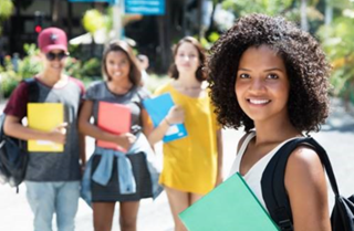 A student with books and her peers standing behind her. 